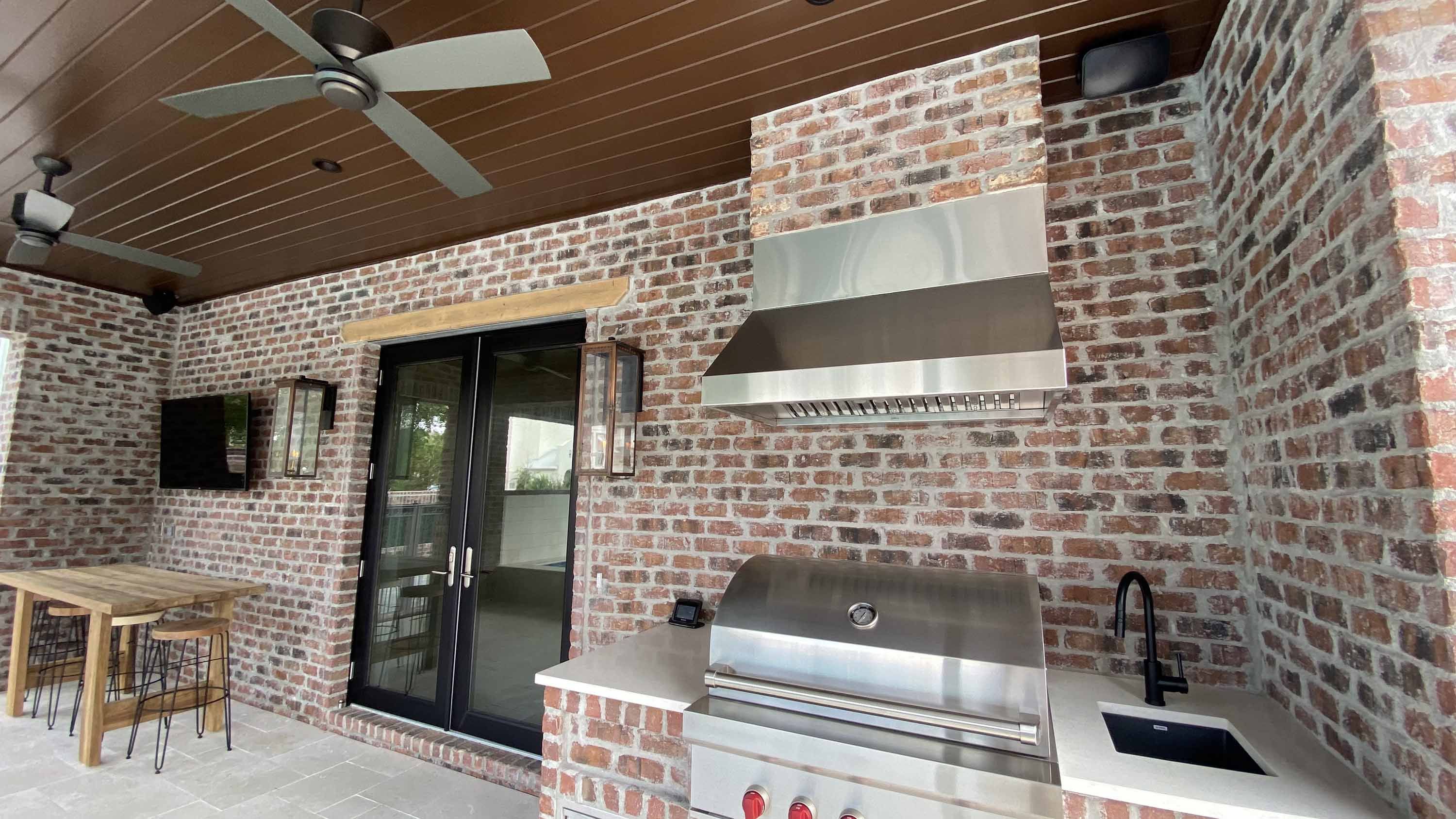 outdoor kitchen area with weatherproof tv and brick walls